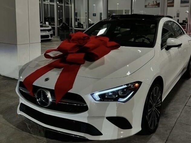 White Mercedes-Benz car with a large red gift bow on the hood displayed on a laptop screen in a website editor.