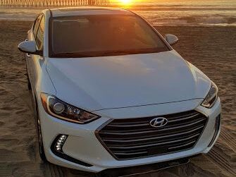 Front view of a white Hyundai Elantra parked near a beach at sunset.